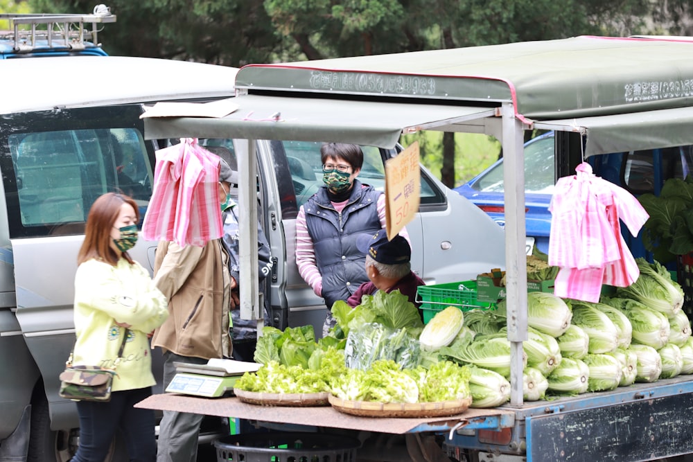 a group of people standing next to a truck filled with vegetables