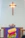 blurred image of a church interior with a wooden crucifix mounted on a wall, above an altar adorned with a purple cloth featuring a design of four glowing candles and some floral decoration.