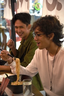 A cheerful group of friends sharing plates of tempura and ramen around a lively table.