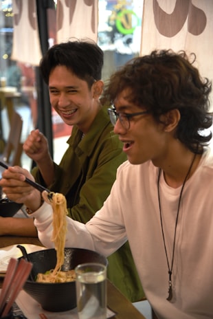 A cheerful group of friends sharing plates of tempura and ramen around a lively table.