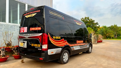 A sleek navy 16-seater luxury minibus parked outside a modern office building.