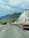 A long line of trucks is parked on a highway. The road stretches into the distance, bordered by rolling hills covered with green vegetation. The sky is cloudy, suggesting overcast weather. One truck is prominently visible with the branding 'euroberry' on its side.