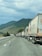 A long line of trucks is parked on a highway. The road stretches into the distance, bordered by rolling hills covered with green vegetation. The sky is cloudy, suggesting overcast weather. One truck is prominently visible with the branding 'euroberry' on its side.