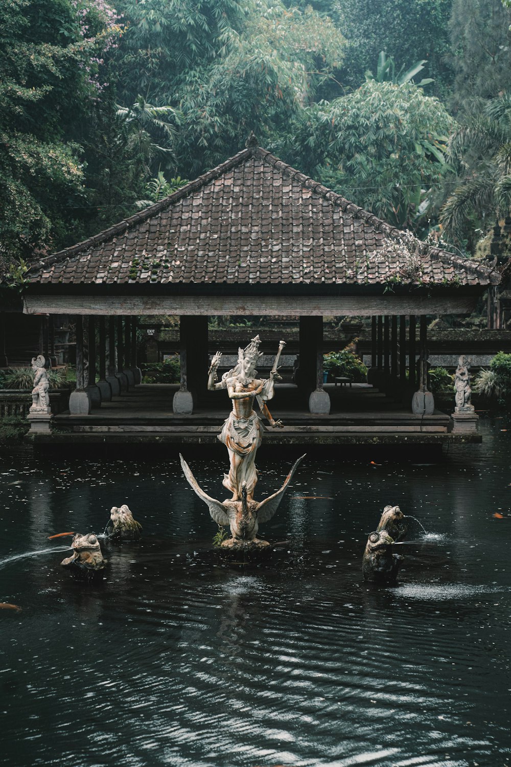 a pond with statues in it and a gazebo in the background