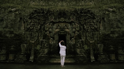 A lone figure standing before a towering doorway carved with mythical symbols.