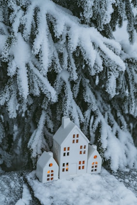 A cozy winter-themed hand-painted plaque featuring a small house surrounded by snow and pine trees.