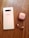 A smartphone placed on a wooden surface alongside a pair of wireless earbuds and their charging case. The phone is white with a triple camera setup. The earbuds and case are metallic copper, reflecting light.