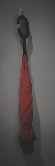 A sleek black umbrella with a wooden handle resting against a rustic brick wall.