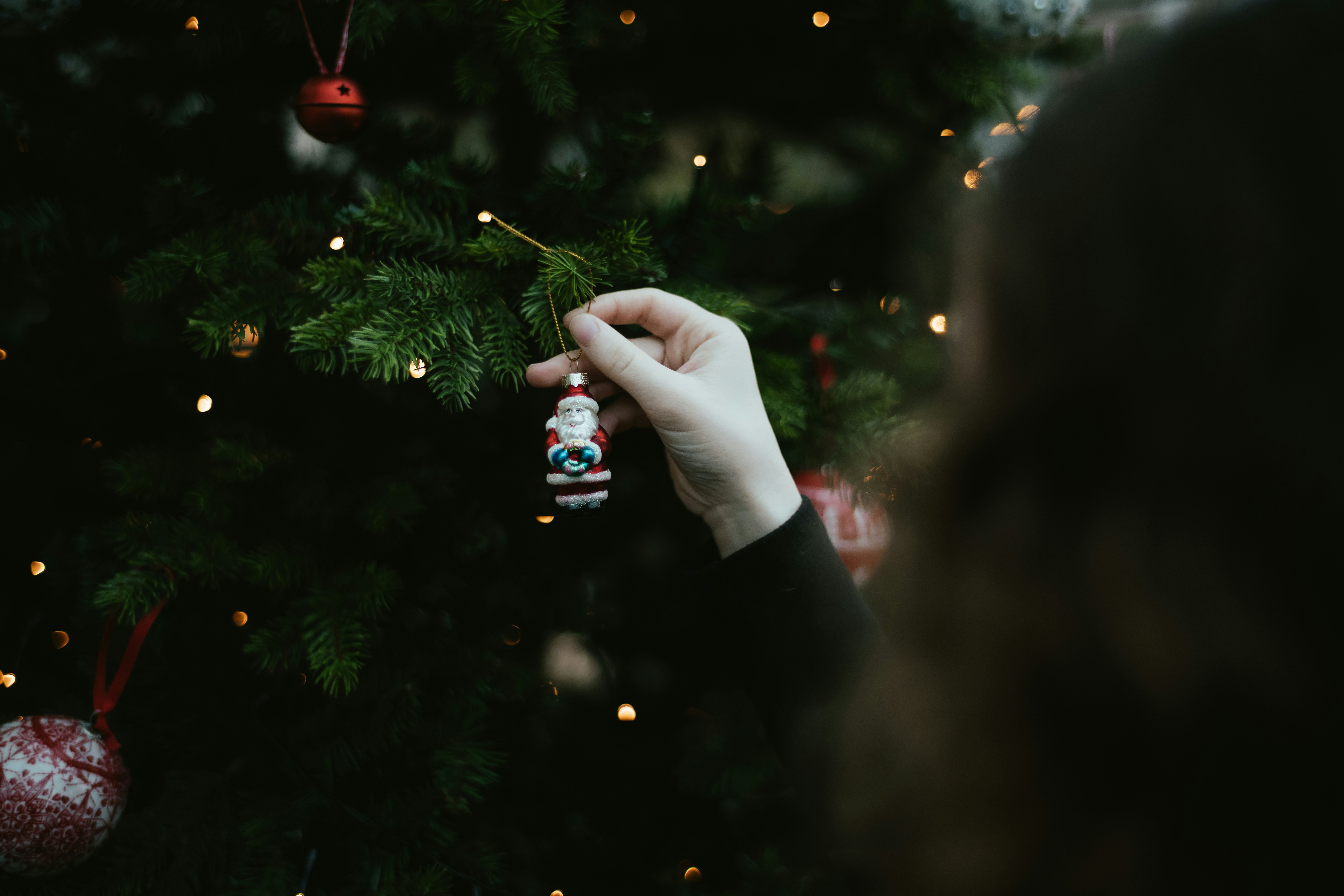Una persona che tiene un ornamento natalizio davanti a un albero di Natale