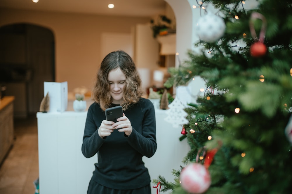 a woman standing in front of a christmas tree looking at her cell phone