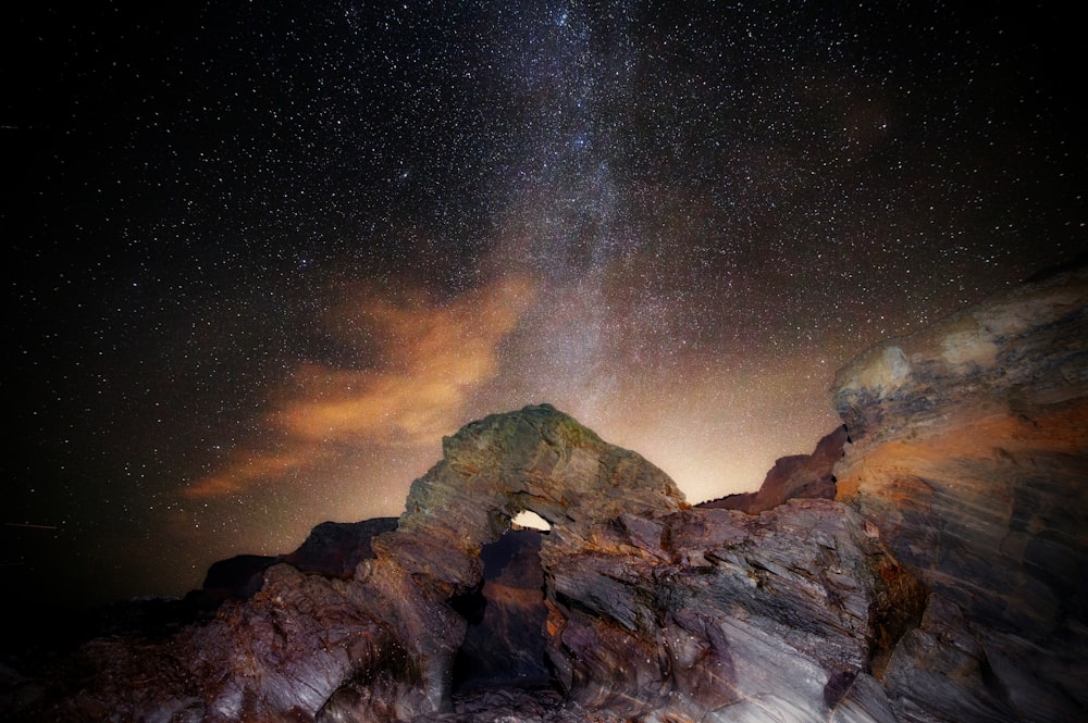the night sky with stars above a rocky outcropping