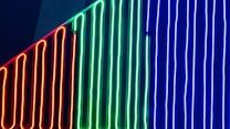 Vertical neon lights in red, green, and blue are arranged in parallel lines against a dark background, creating a vibrant and modern aesthetic.