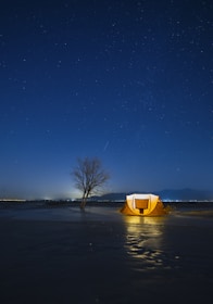 A panoramic shot of a lone tent under a star-packed sky beside a quiet mountain stream