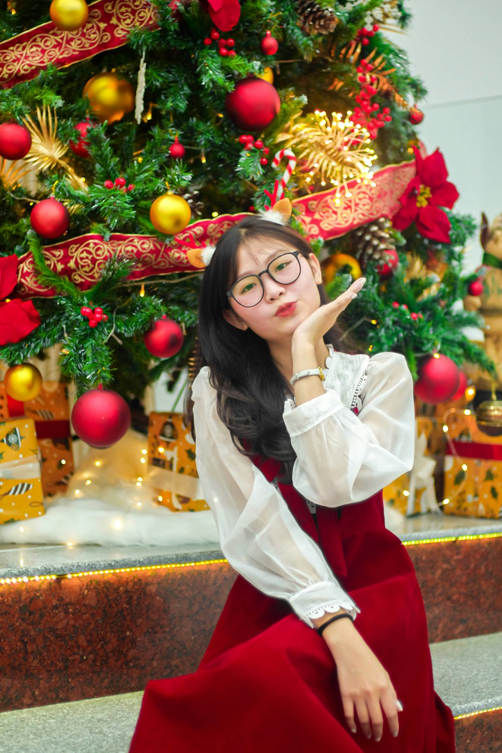 a woman in a red dress sitting in front of a christmas tree