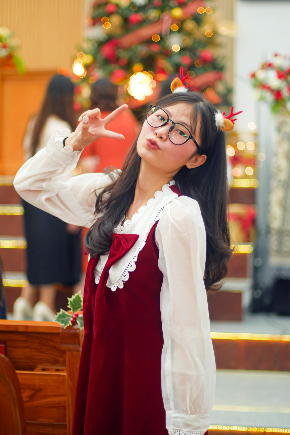 a woman wearing glasses standing in front of a christmas tree