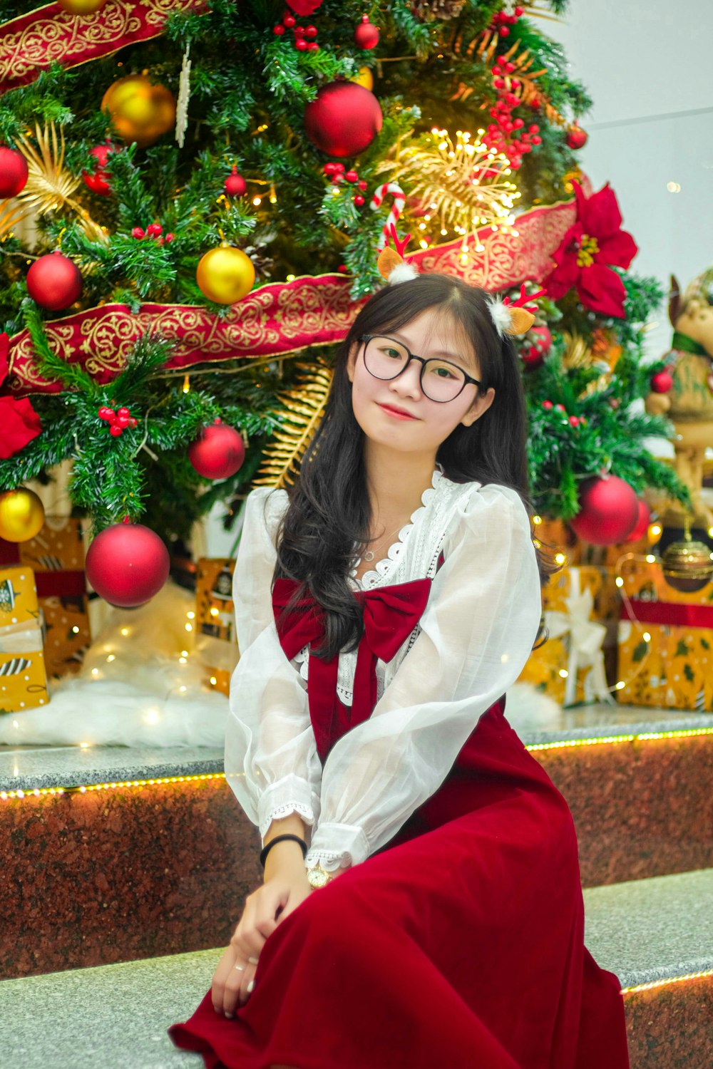 a woman in a red dress sitting in front of a christmas tree