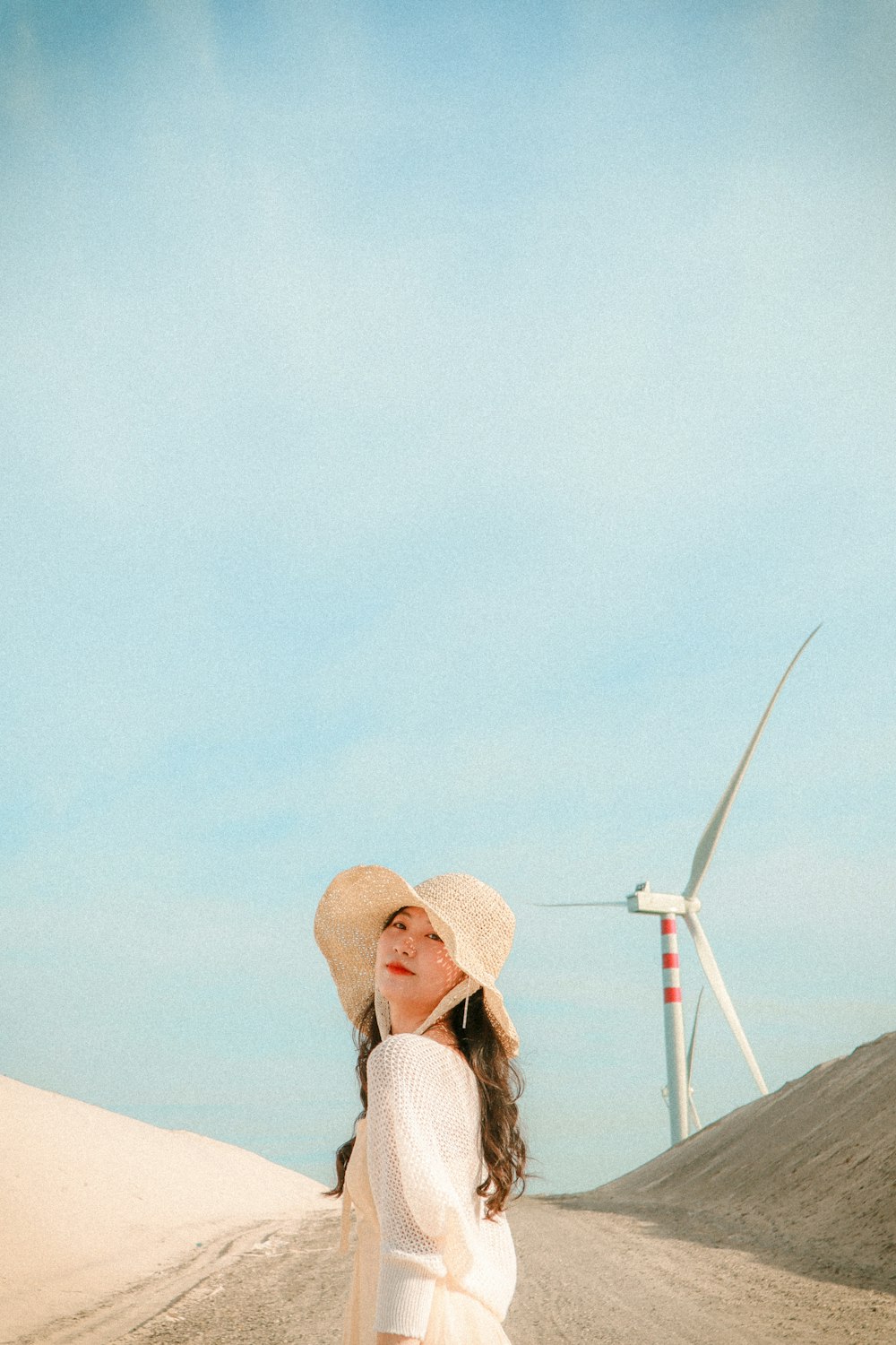 a woman in a white dress and hat standing in the sand