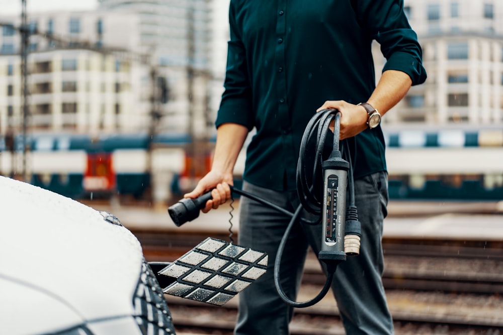 a man standing next to a white car with a power cord attached to it