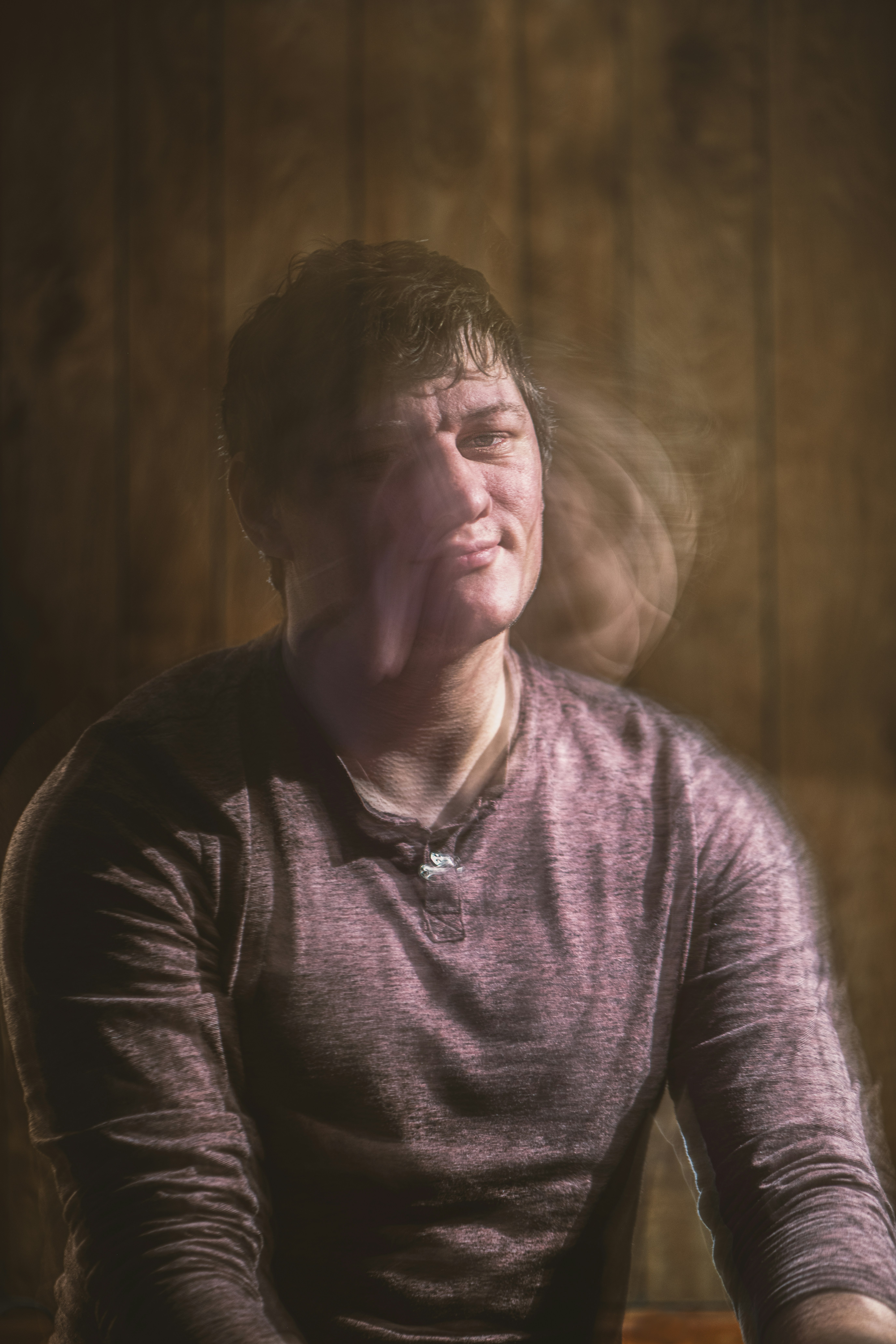 a man sitting in front of a wooden wall smoking a cigarette
