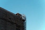 A modern building under construction with scaffolding and clear blue sky.