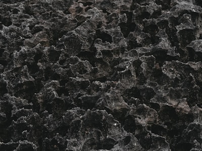 A textured surface resembling rough, dark, volcanic rock with an uneven pattern.