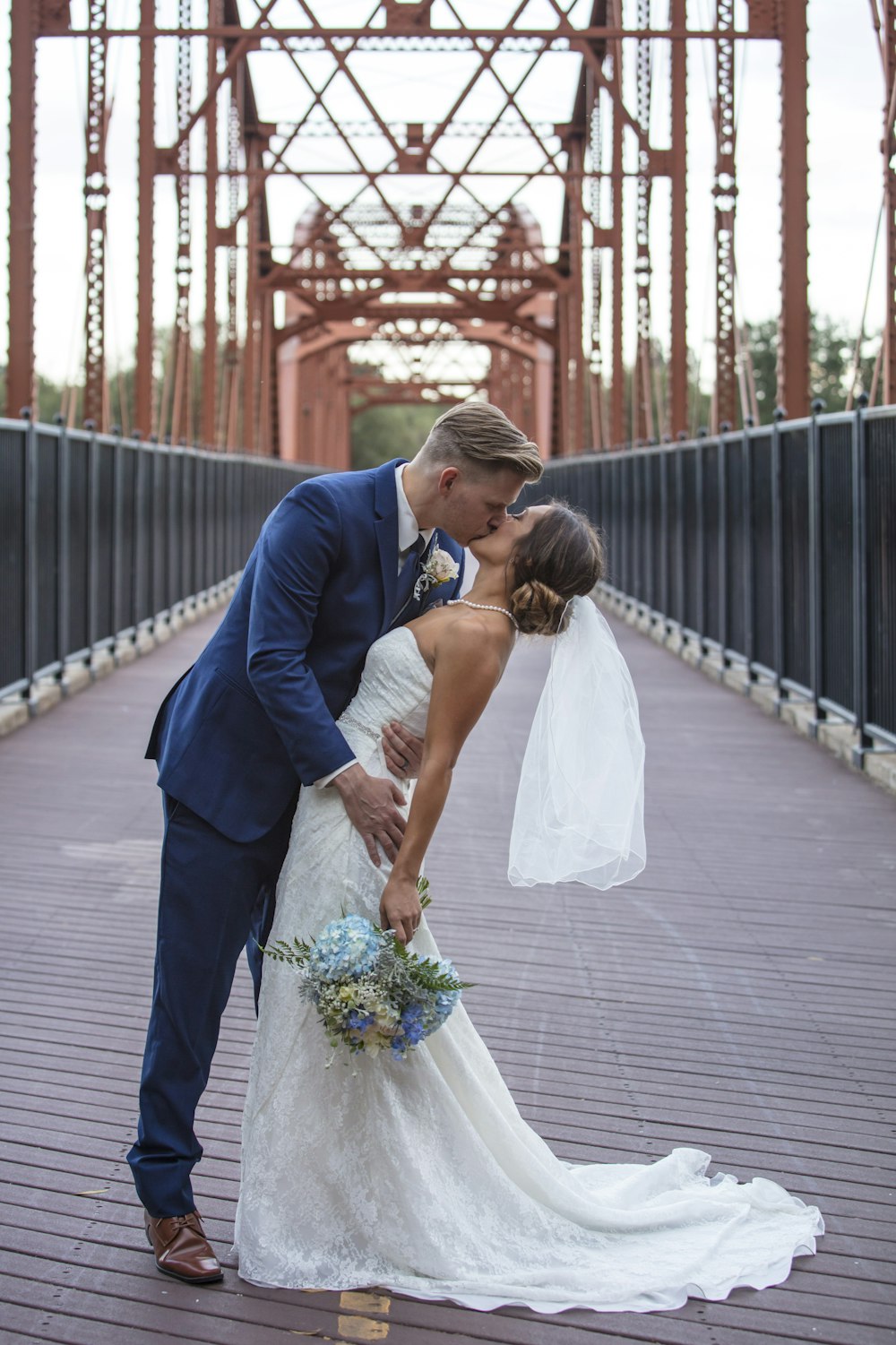 a bride and groom kissing on a bridge