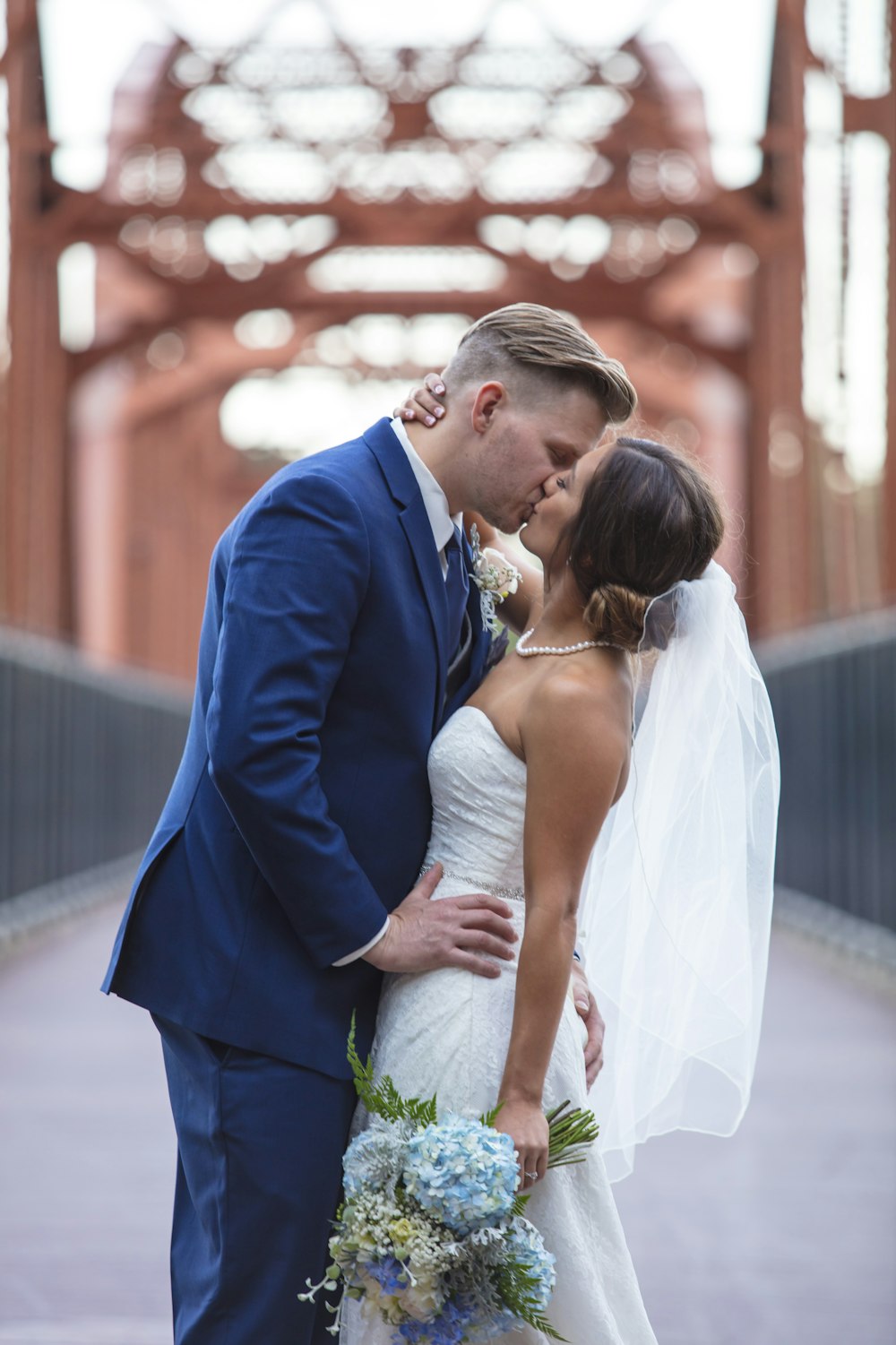 a bride and groom kissing on a bridge