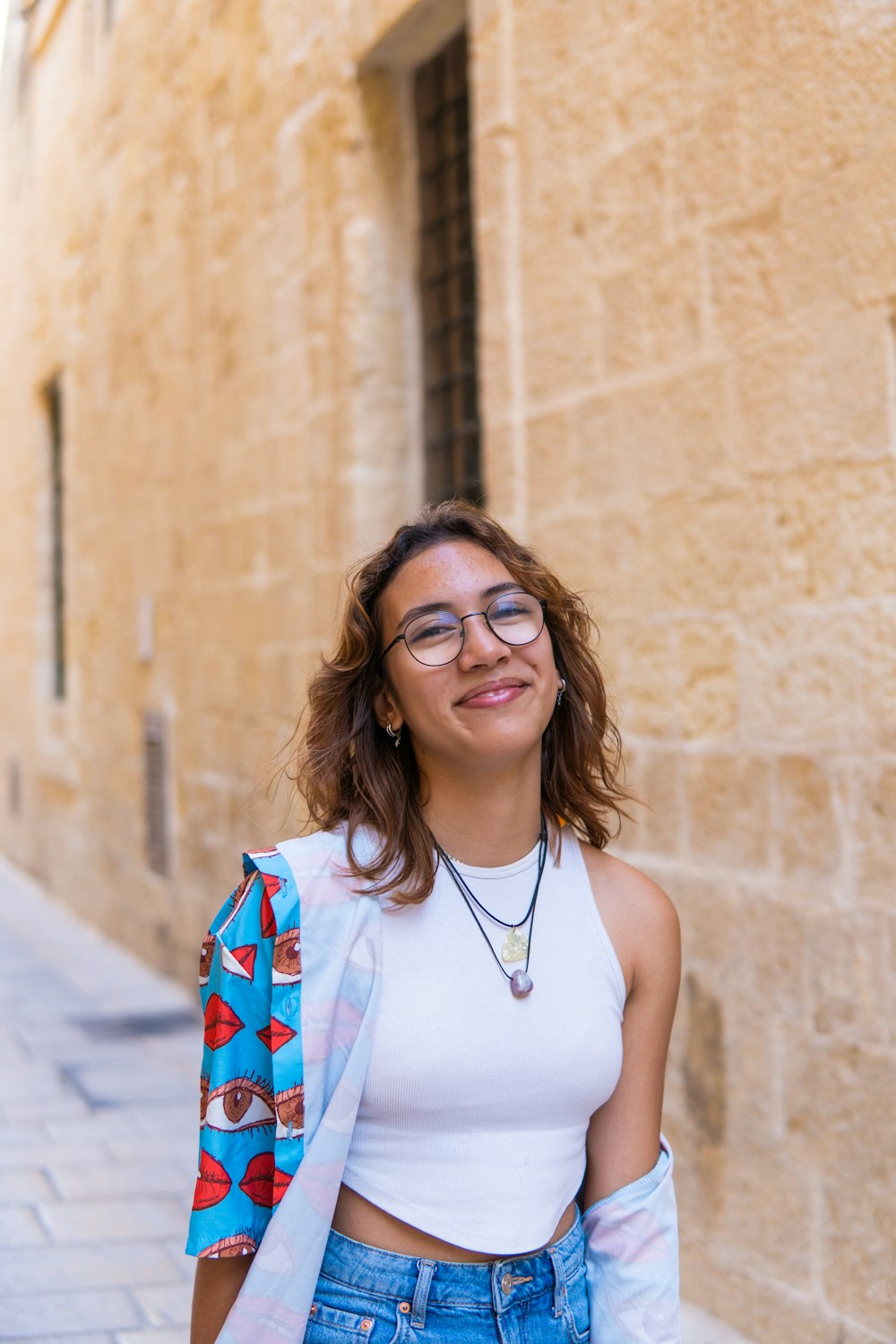 a woman wearing glasses and a white top standing in front of a building