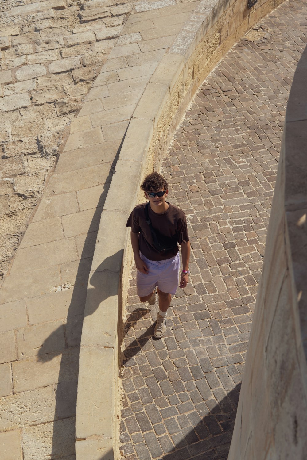 a man walking down a brick walkway next to a stone wall