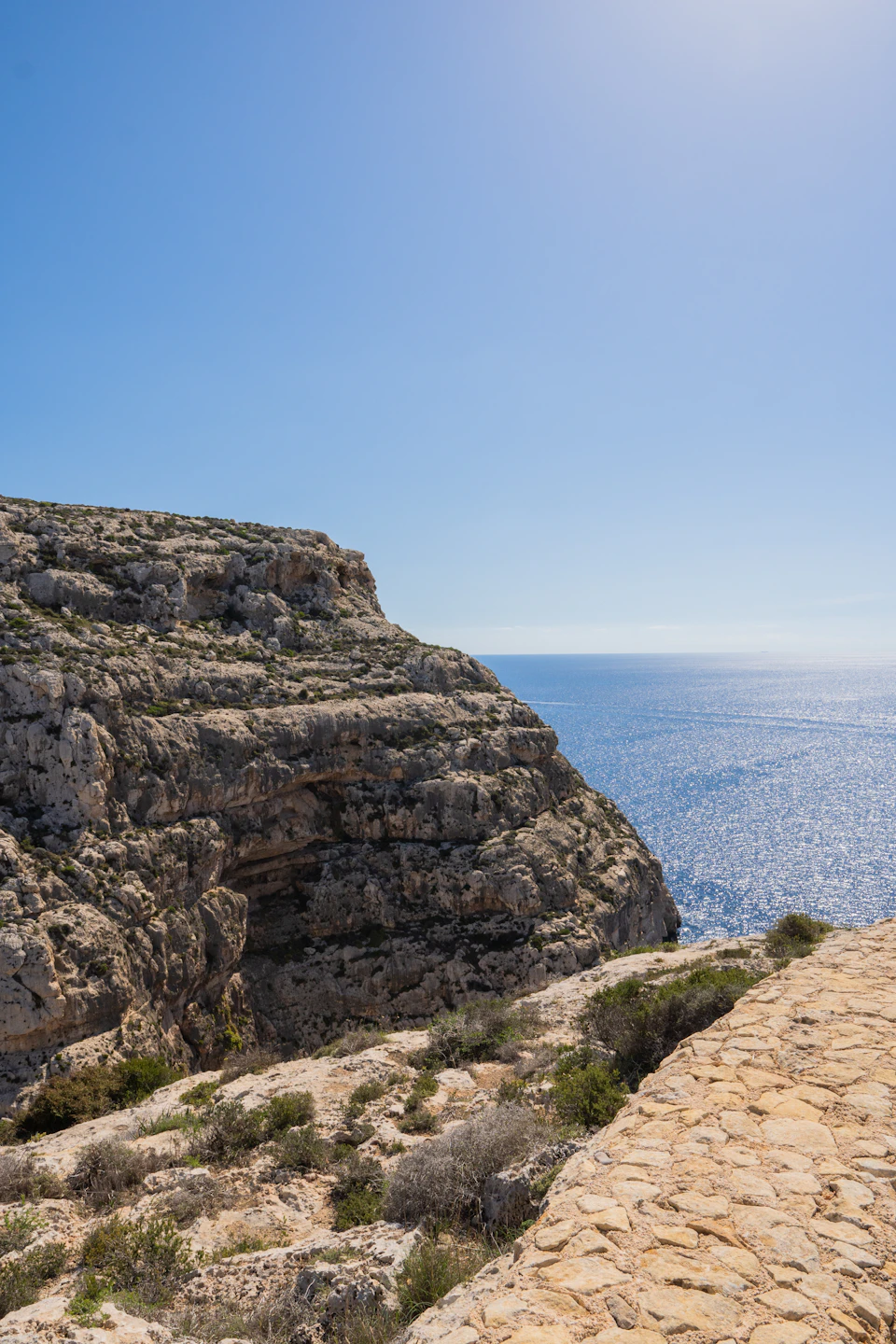 Rocky cliff face with vegetation at its base, surrounded by clear blue sky above