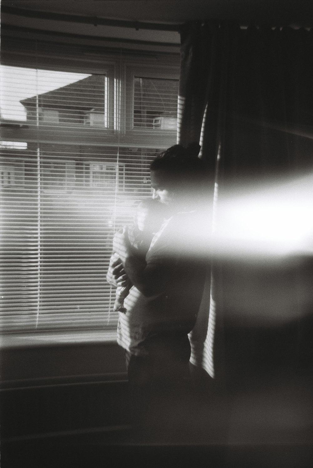 a black and white photo of a person standing in front of a window