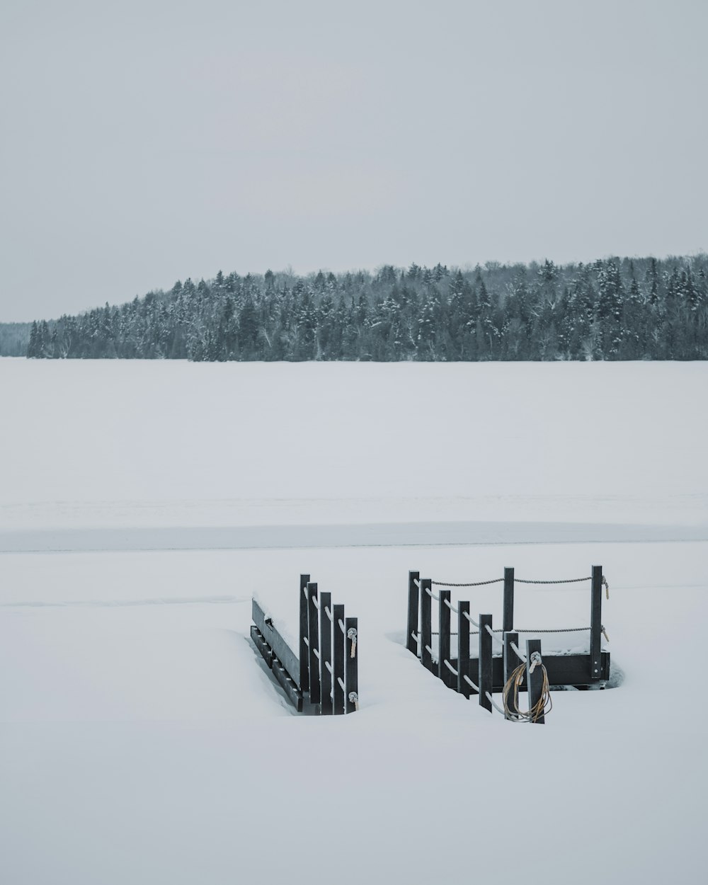 a snow covered field with a fence and trees in the background