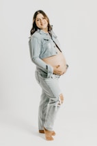 A smiling mother wearing comfortable maternity clothes standing next to a rack of stylish baby outfits.