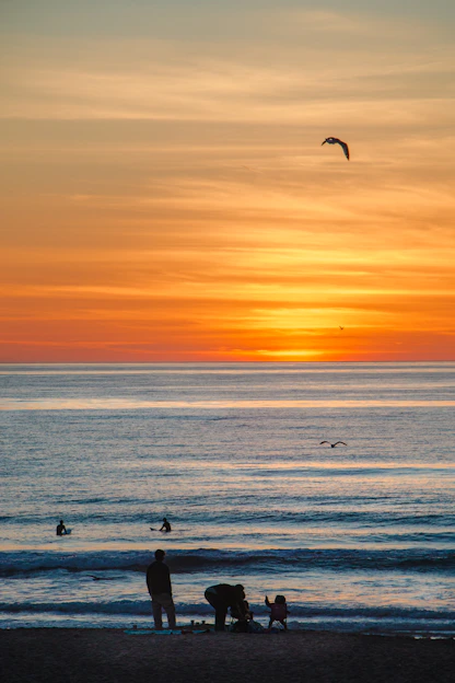 A vibrant beach scene in California with surfers catching waves at sunset.