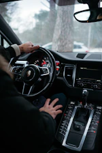 Close-up of hands gripping a steering wheel inside a modern car with a clear road ahead.