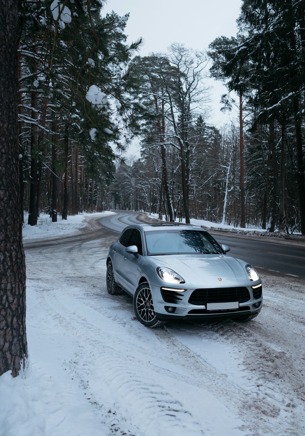 a silver sports car driving down a snow covered road