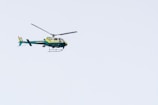 A green and yellow helicopter marked with the word 'Sheriff' is flying in a clear blue sky. The helicopter's rotors are spinning and it has a tail rotor for stabilization.
