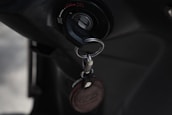 A close-up of an ignition switch with a key inserted, accompanied by a keychain with a leather tag. The setting appears to be dark, emphasizing the metallic and leather textures.