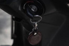 A close-up of an ignition switch with a key inserted, accompanied by a keychain with a leather tag. The setting appears to be dark, emphasizing the metallic and leather textures.