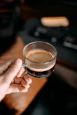 Close-up of hands typing on a keyboard with a cup of espresso nearby.