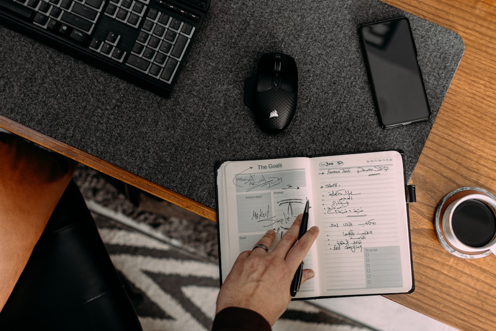 a person is writing on a notebook next to a keyboard