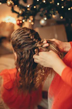 A joyful princess host braiding a little girl's hair with colorful ribbons in a bright, decorated room.