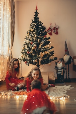 two girls sitting on the floor in front of a christmas tree