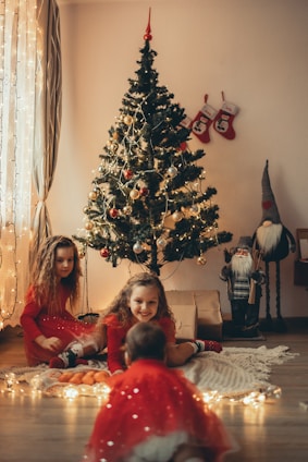 two girls sitting on the floor in front of a christmas tree