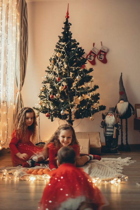 two girls sitting on the floor in front of a christmas tree