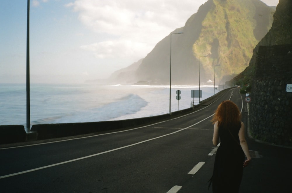 a woman walking down a road next to the ocean