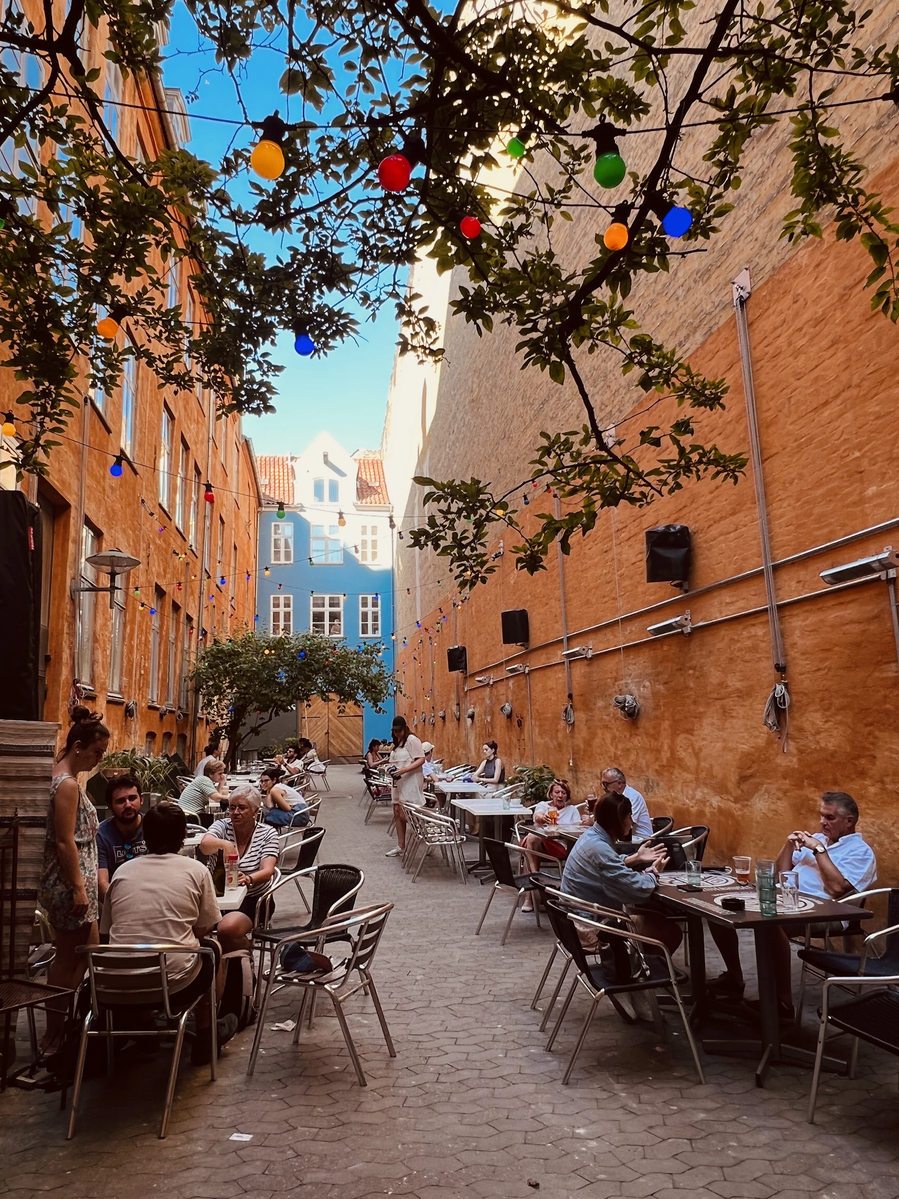 A warm neighborhood alley strung with lights, lined with restaurants and people dining outdoors