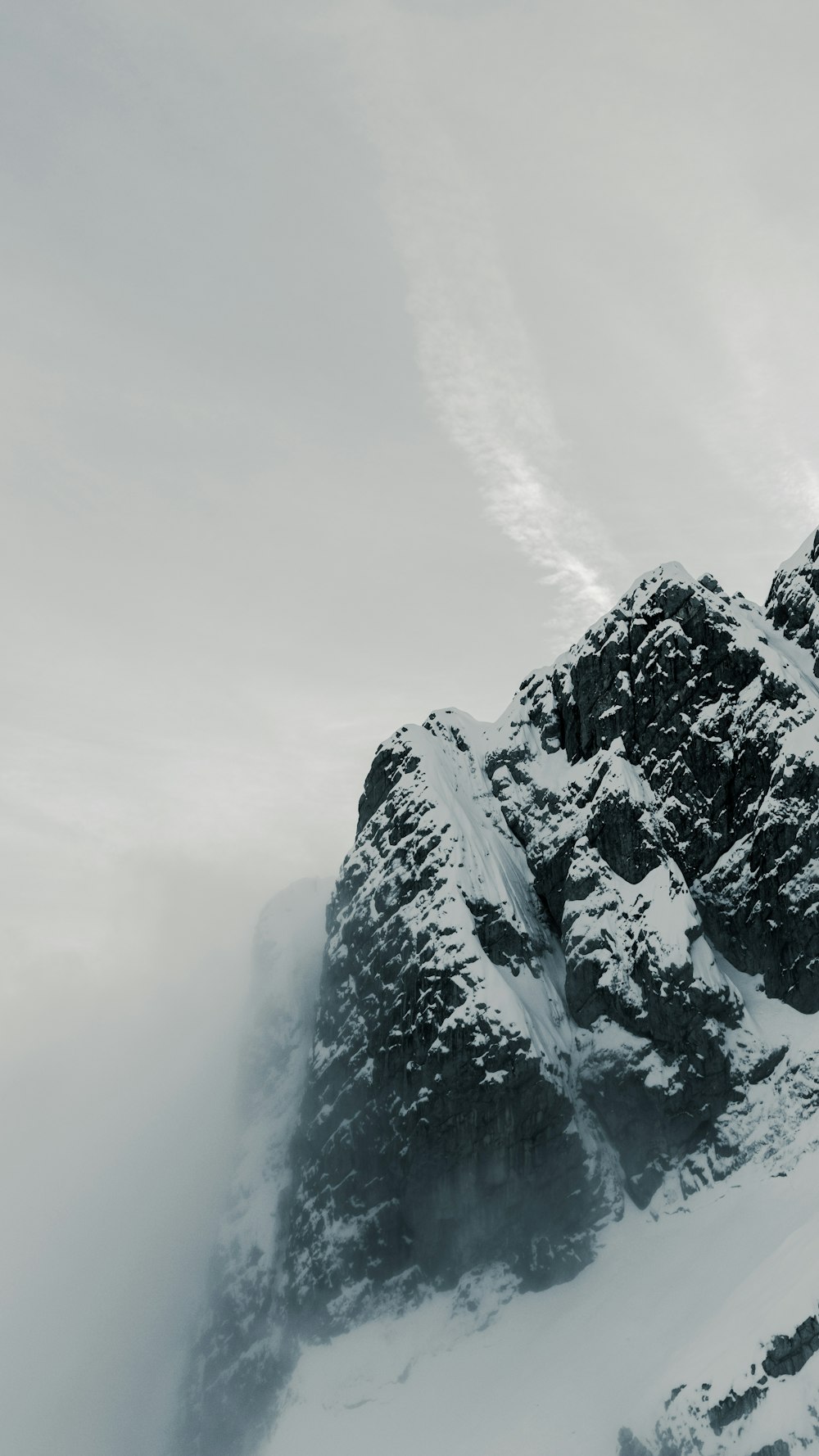 a very tall mountain covered in snow under a cloudy sky