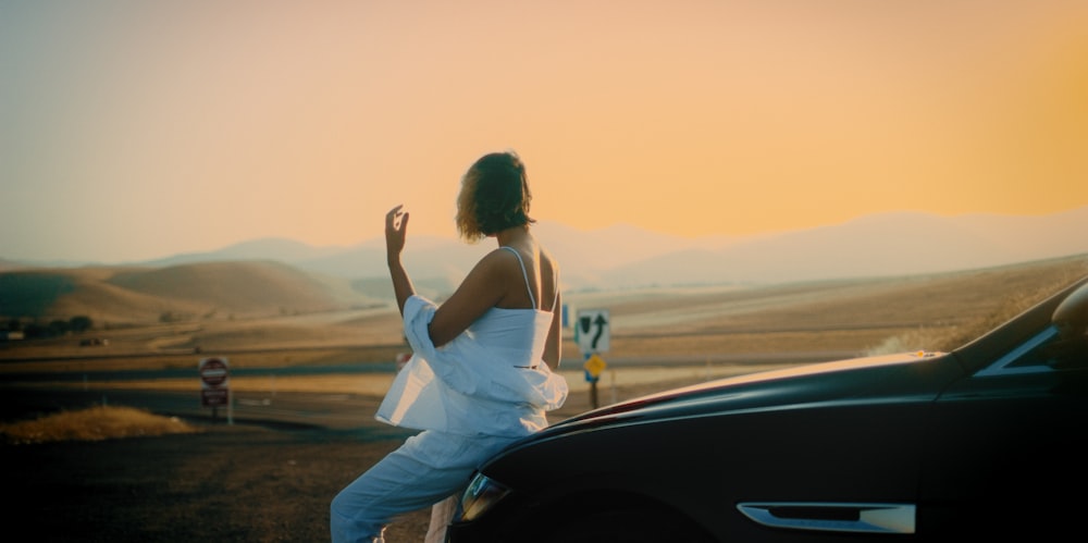 a woman in a white dress standing next to a car