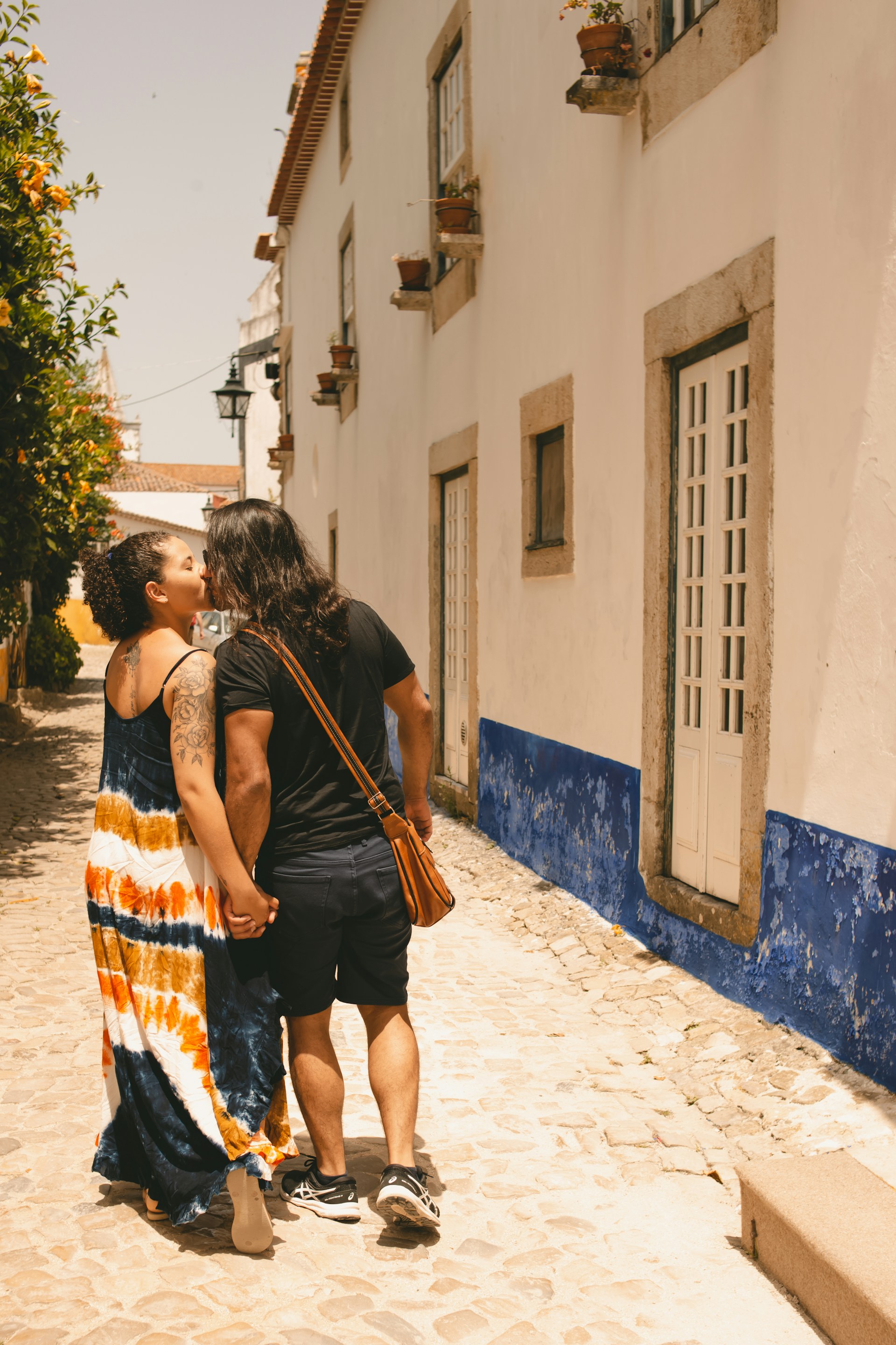 An elegant cinematic shot of a couple walking hand in hand along the cobblestone streets of a quaint French village at golden hour.